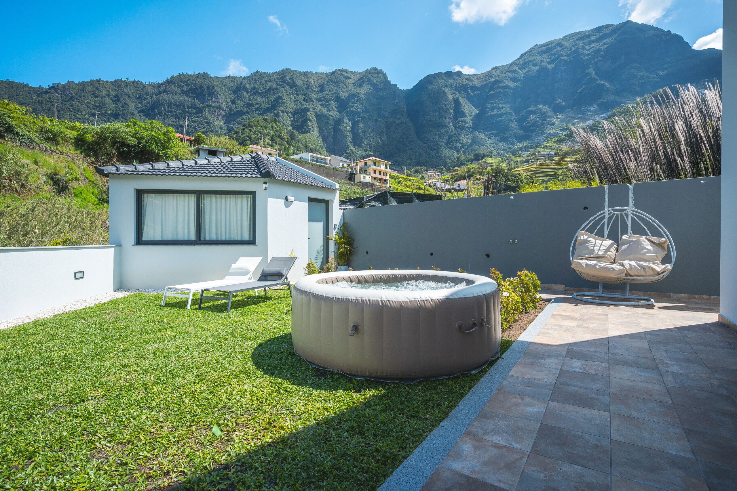 A modern outdoor patio with a hot tub, lounge chairs, and a view of a mountainous landscape.