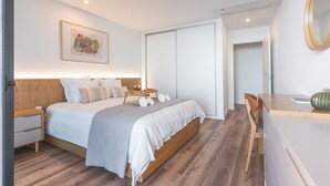A modern bedroom with a wooden bed, a bedside table, a chair, a desk, and a mirror.