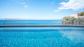 A clear blue pool with a metal fence and a view of the ocean.