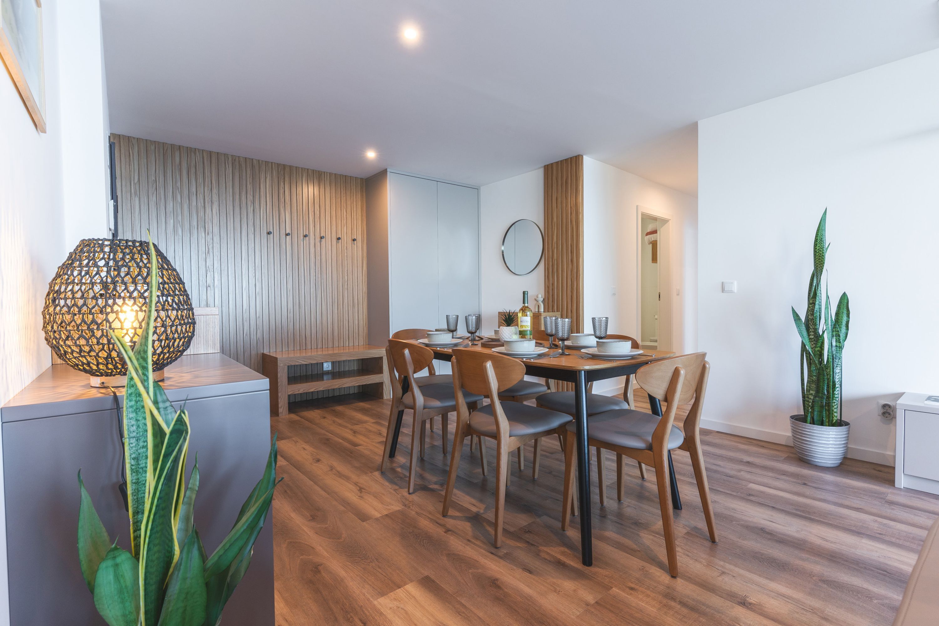 Un comedor moderno con una mesa y sillas de madera, una planta en maceta y una lámpara decorativa.