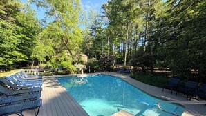 A swimming pool with a wooden deck, lounge chairs, and surrounding trees. - Winnipesaukee Condo Walk to Beach, Pool, Near Gunstock (Gilford)
