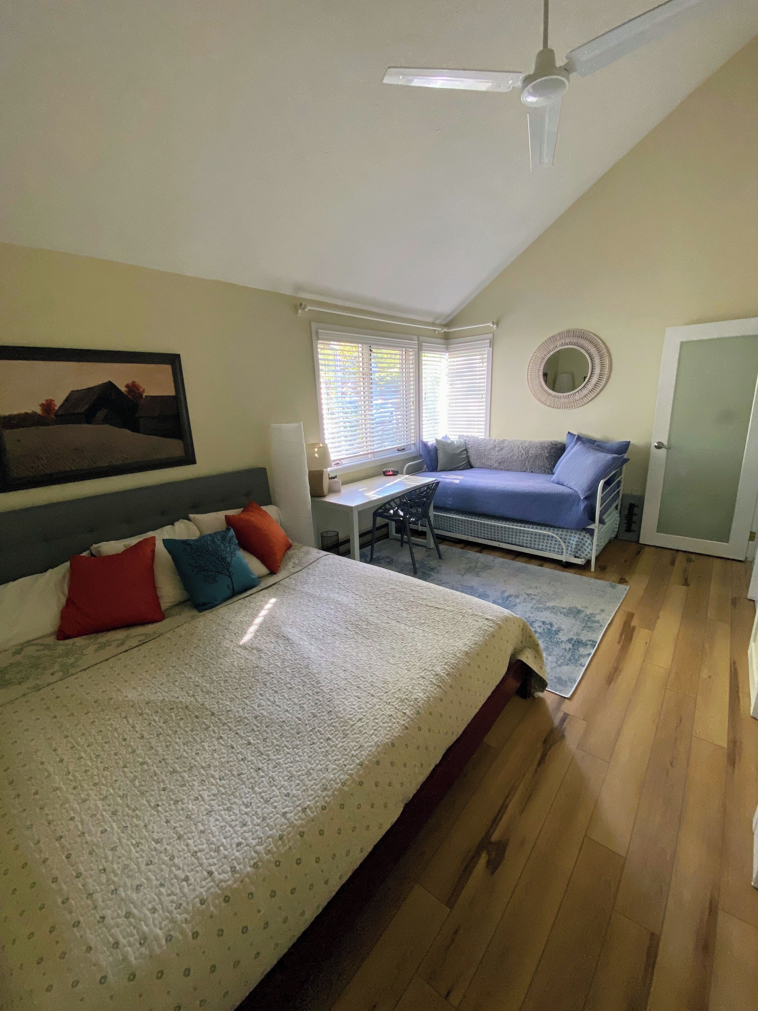 A bedroom with a bed, a desk, a chair, a ceiling fan, and a window with blinds.