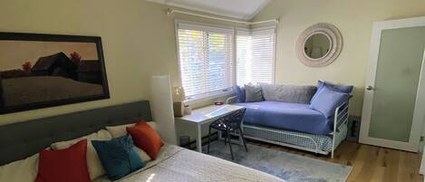 A bedroom with a bed, a desk, a chair, a ceiling fan, and a window with blinds.