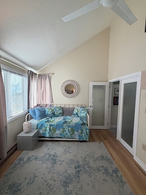Um quarto com cama, um ventilador de teto, janela com persianas, uma porta e um tapete.