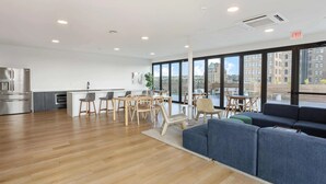 A modern kitchen with stainless steel appliances, a dining area with wooden chairs and tables, and a large window offering a city view. - Optimum - Downtown Oasis! (Birmingham)
