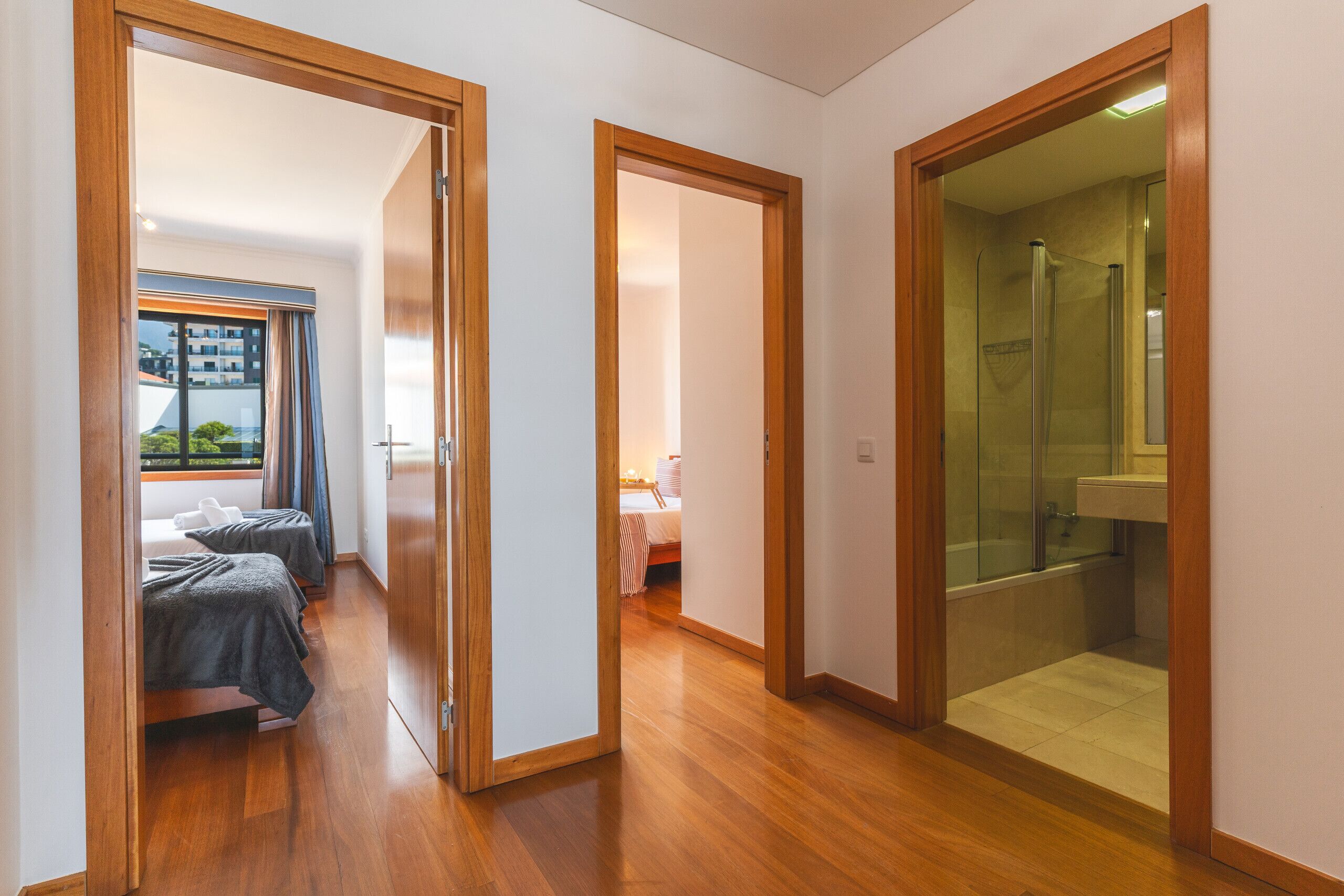 A hotel room with a wooden floor, a glass shower, and a bed with a view of the outside.