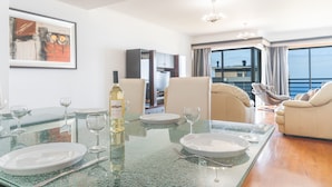 Comedor con una mesa de vidrio preparada para cuatro, una botella de vino blanco y un cuadro en la pared.
