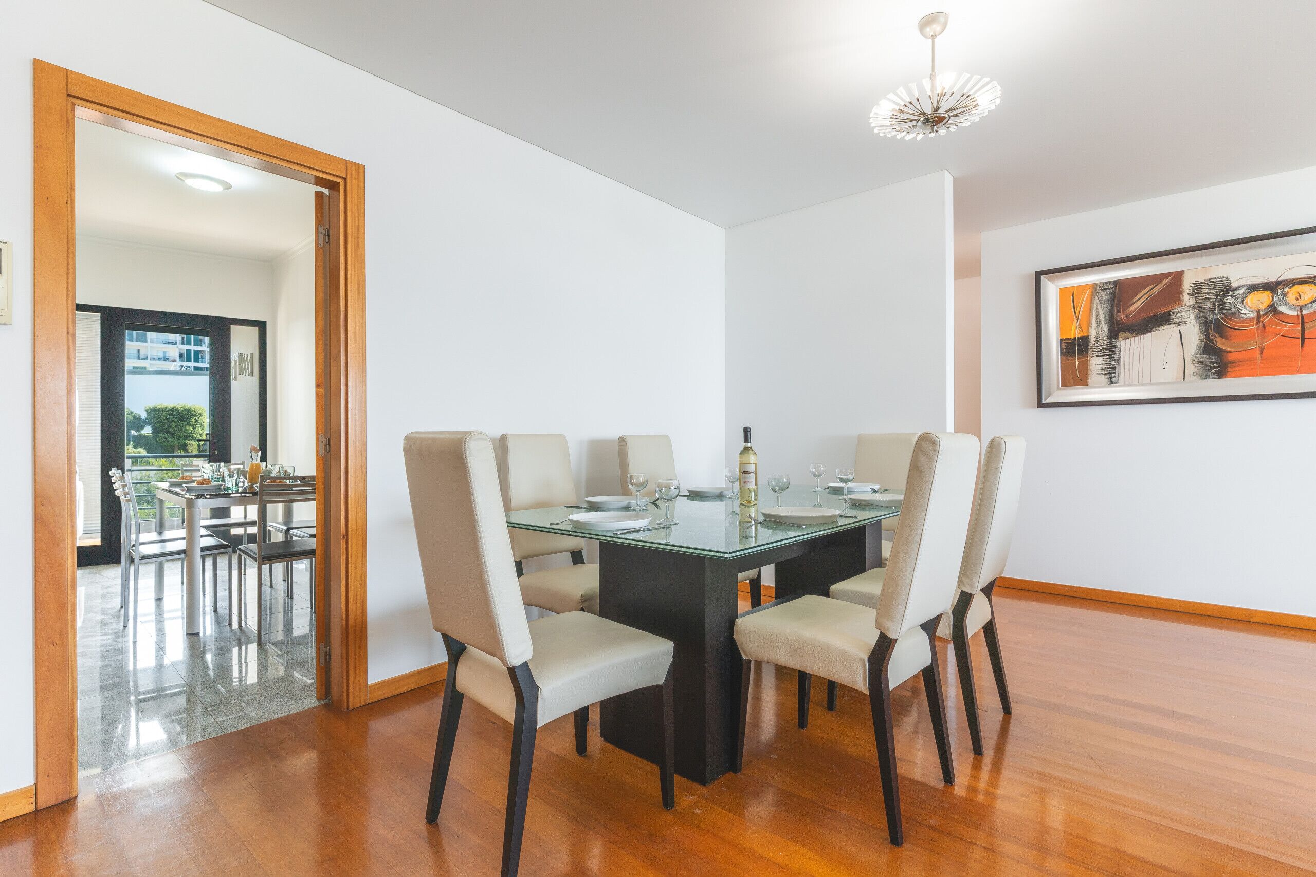 Uma sala de jantar com mesa de vidro, seis cadeiras e uma garrafa de vinho.