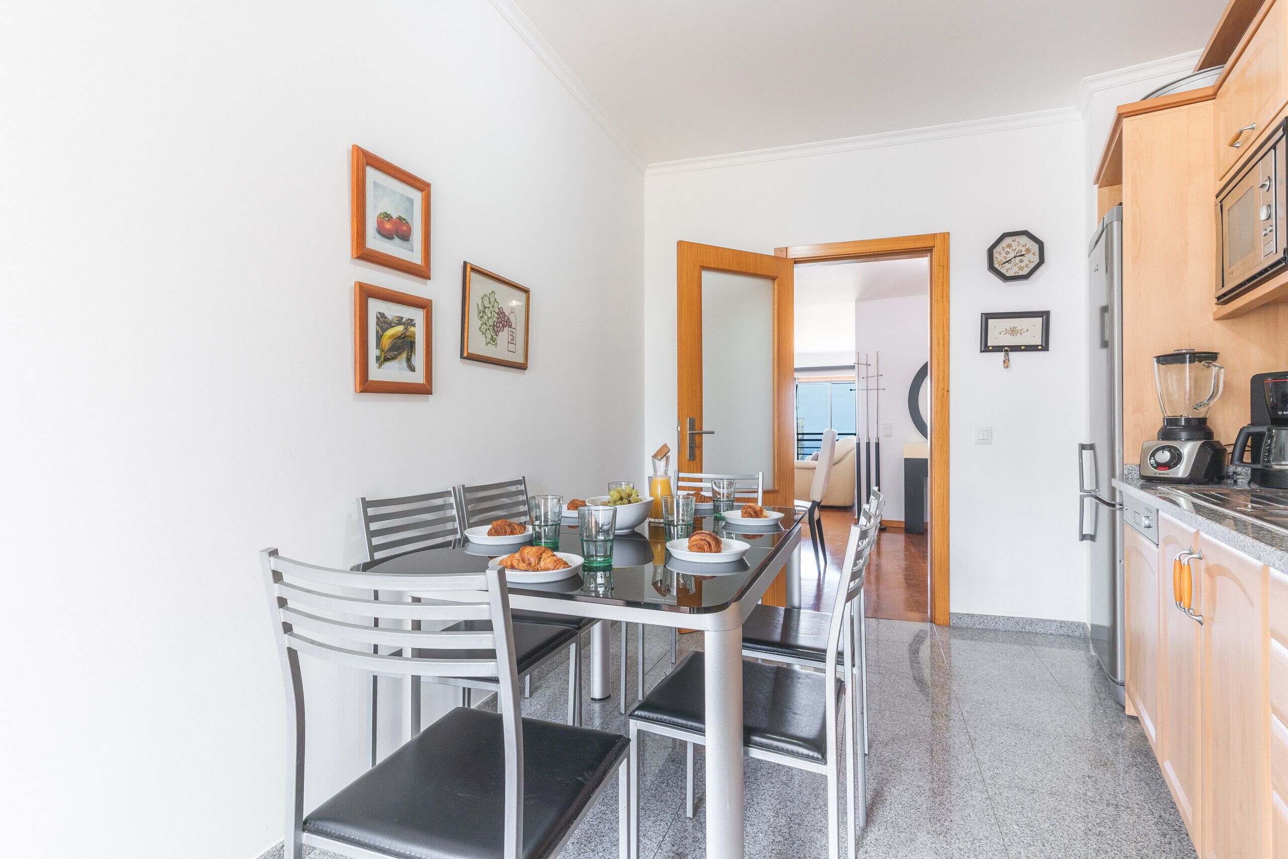 A dining area with a table set for four, chairs, and a kitchen with appliances.