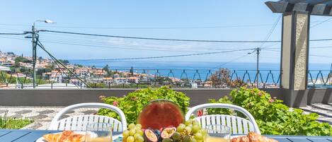 A table with a plate of food, a glass of juice, and a view of the sea and town.