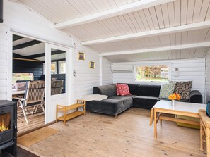 A cozy living room with a fireplace, a sofa, a dining table, and a window with a view. - 6 Person Holiday Home in Haderslev (Haderslev)
