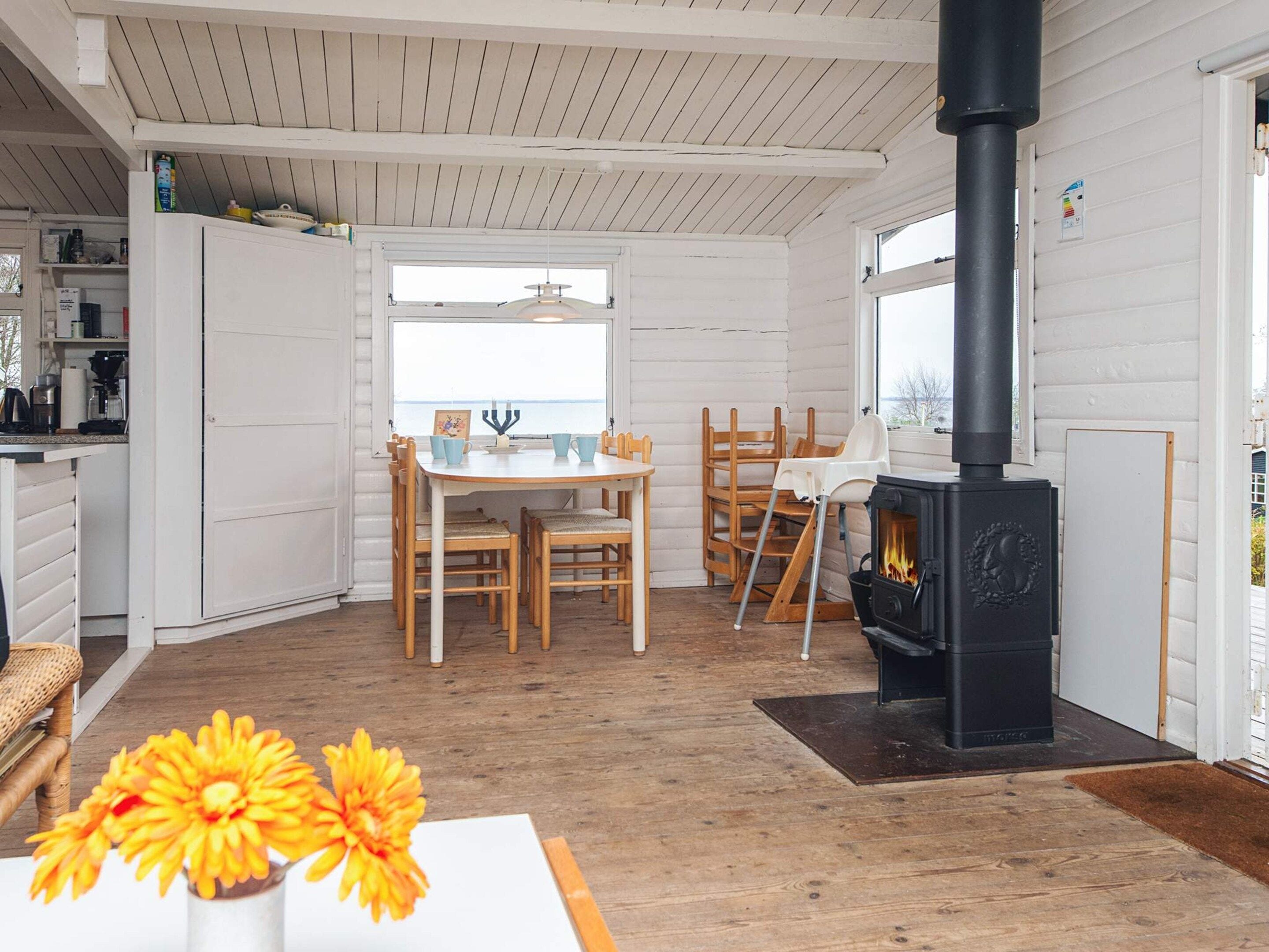 A cozy room with a wooden floor, a dining table with chairs, a white cabinet, and a black wood-burning stove.