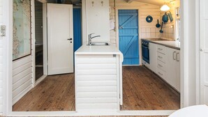 Una cocina compacta con armarios blancos, una puerta azul y suelo de madera.