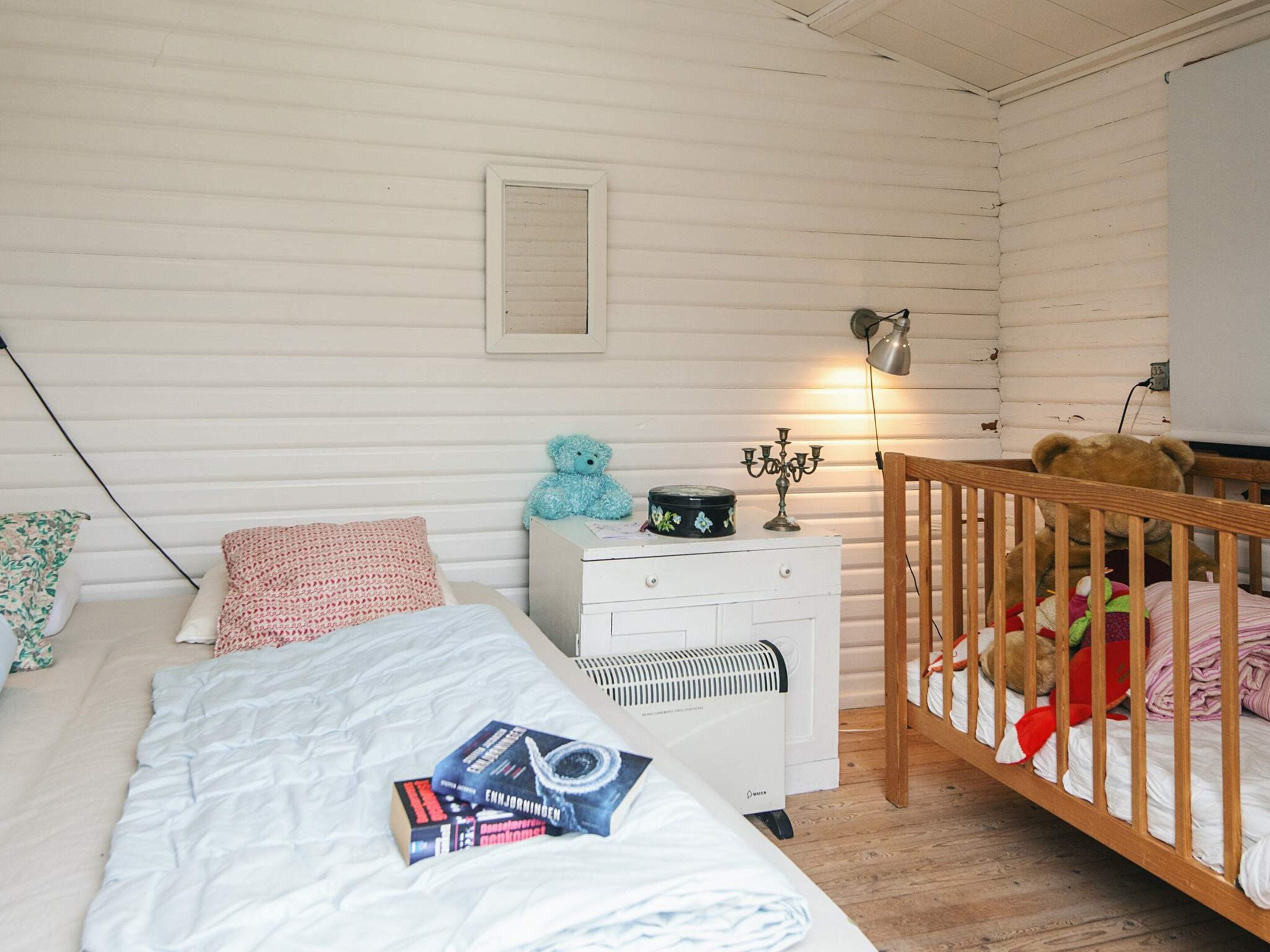 A bedroom with a bed, bedside table, lamp, and a crib with a teddy bear.