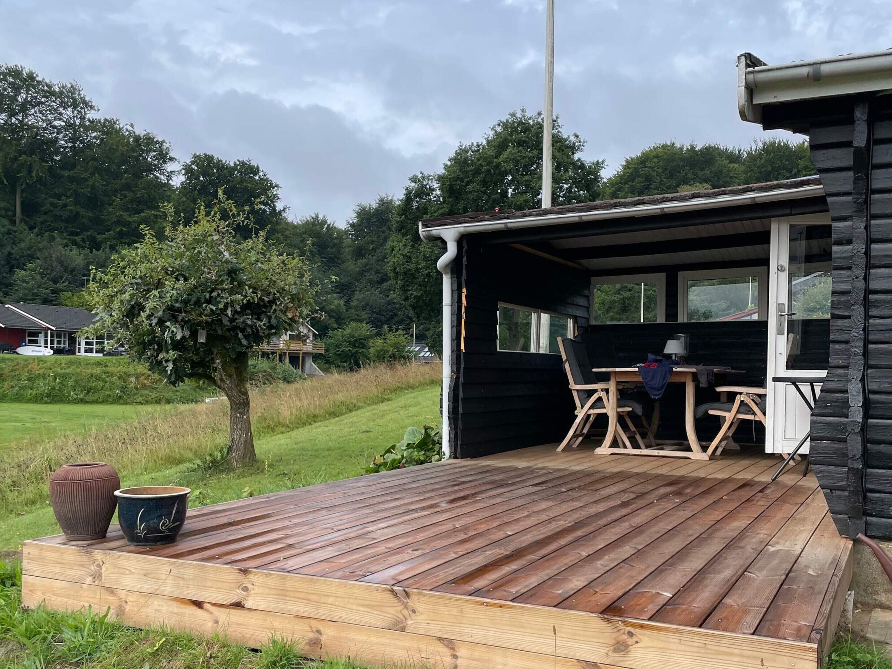 Eine Holzterrasse mit Tisch und Stühlen, ein kleiner Baum und ein Haus im Hintergrund.