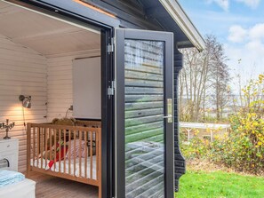 A room with a crib, a bedside table with a lamp, and a view of the outdoors. - 6 Person Holiday Home in Haderslev (Haderslev)
