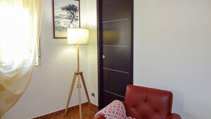 A room with a red chair, a standing floor lamp, a framed picture on the wall, and a dark door.