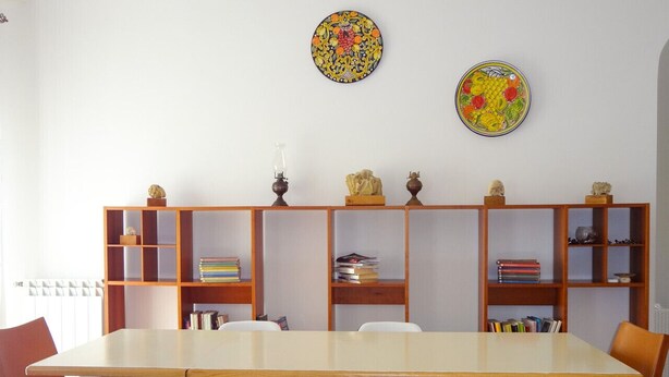 A dining area with a long table, white chairs, and wooden bookshelves filled with books and decorative items.