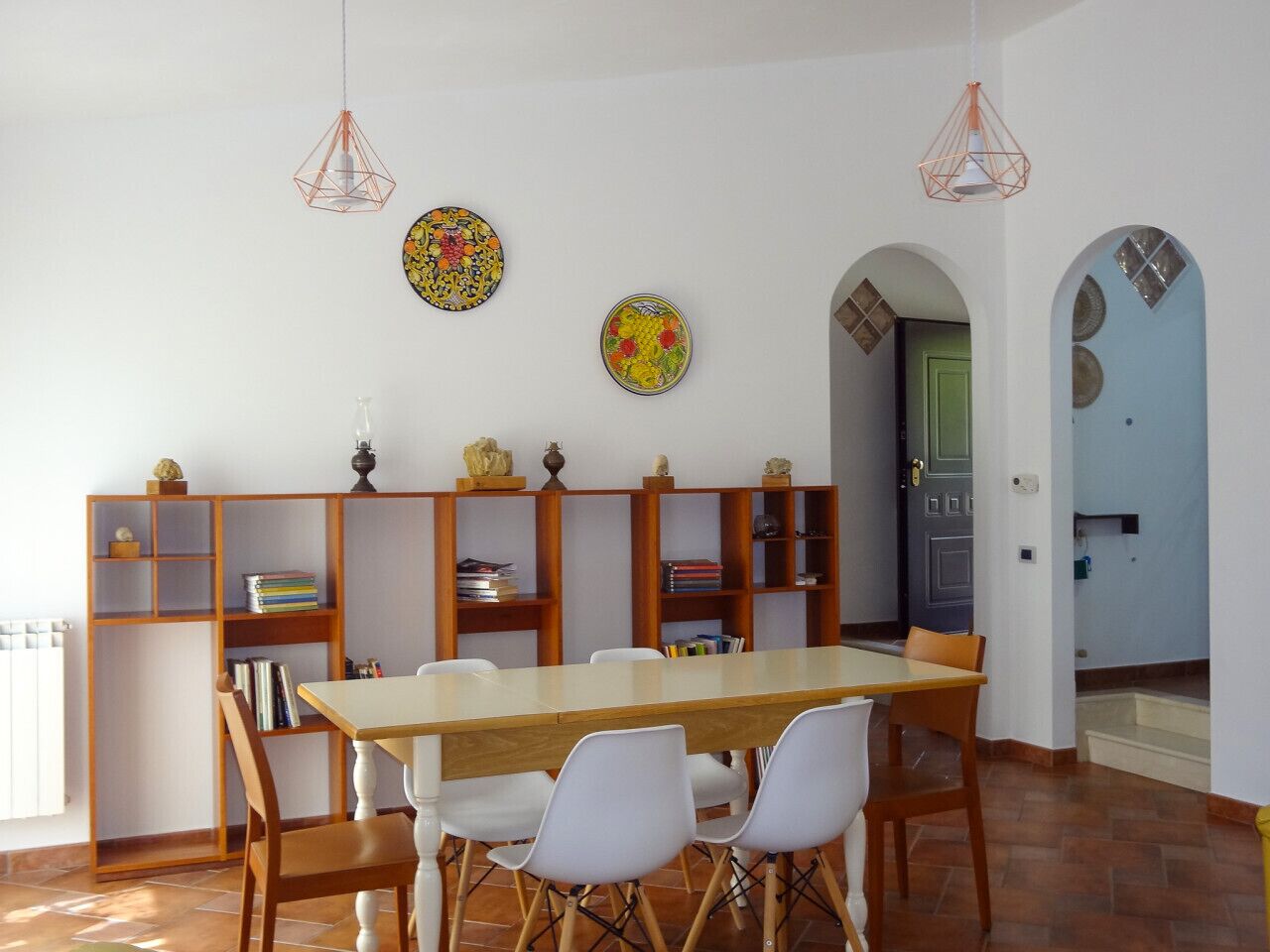 A dining area with a long wooden table, white chairs, and a bookshelf with books and decorative items.