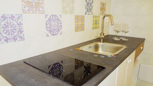 A kitchen with a black countertop, stainless steel sink, and decorative tiles on the backsplash. - Villa the Lily - Apartment Sage (Montallegro)