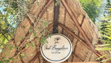 A thatched roof structure with a sign reading 'Ikal Bungalows TULUM.'