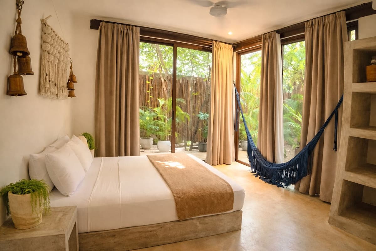 A bedroom with a bed, a hammock, and a view of greenery outside.