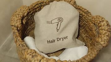 Un panier tressé contenant une serviette blanche et un sac en tissu orné du symbole d’un sèche-cheveux, ainsi que de l’inscription « Sèche-cheveux ».