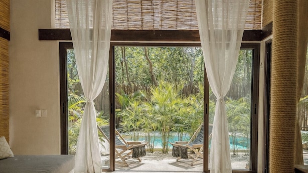 A room with a large glass door leading to a pool area, a sofa, and a view of greenery. - Ikal Bungalows (Tulum)