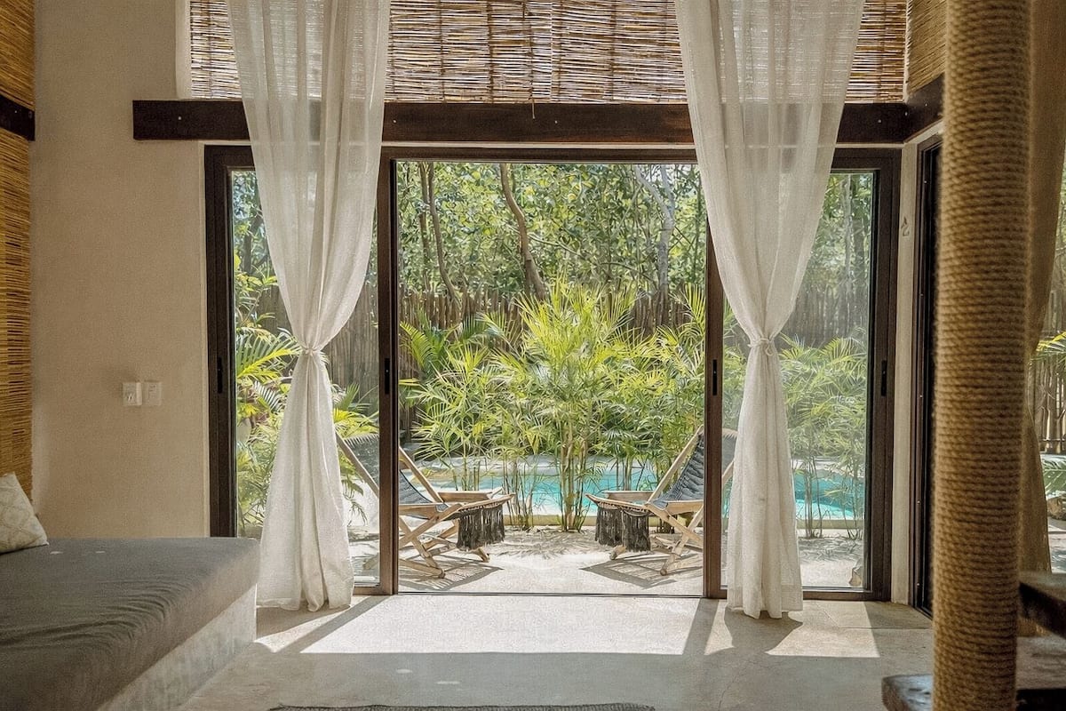 A room with a large glass door leading to a pool area, a sofa, and a view of greenery.