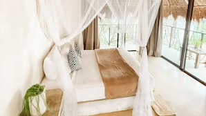 A room with a bed under a thatched roof, large windows, and a view of greenery. - Ikal Bungalows (Tulum)