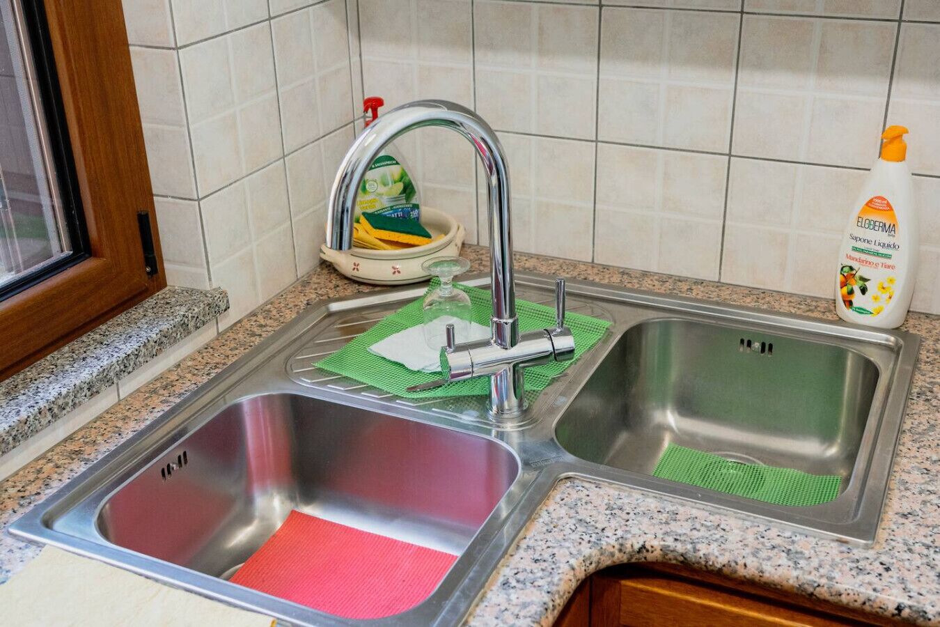 A kitchen with two stainless steel sinks, a faucet, and a bottle of soap on the counter.