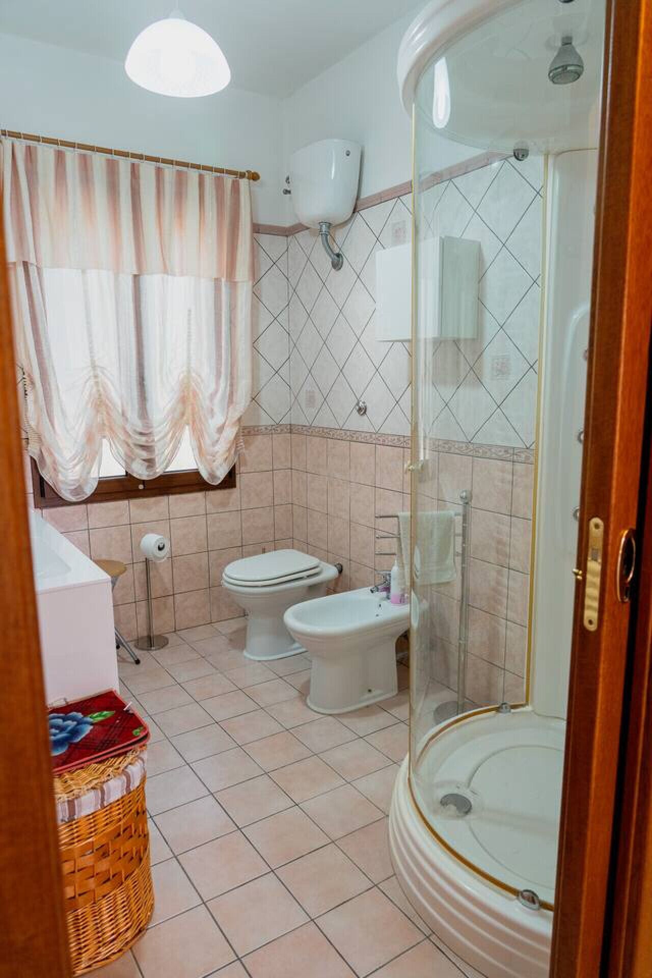 Une salle de bain avec deux toilettes, un espace douche et une fenêtre avec des rideaux.