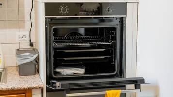 Ein offener Backofen mit Rost und einer Tasche darin, ein Mülleimer und eine Arbeitsplatte mit einem Wasserhahn.