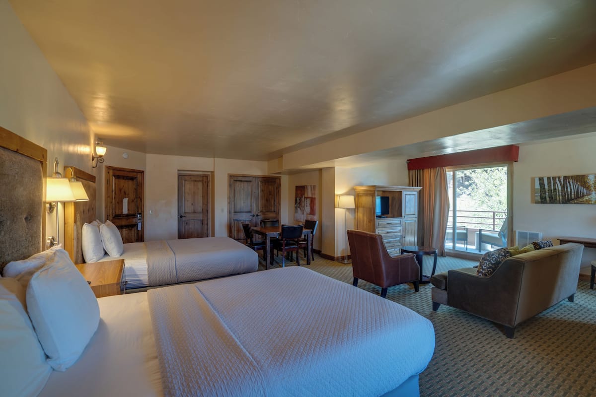 A hotel room with two beds, a desk, a chair, and a sofa.