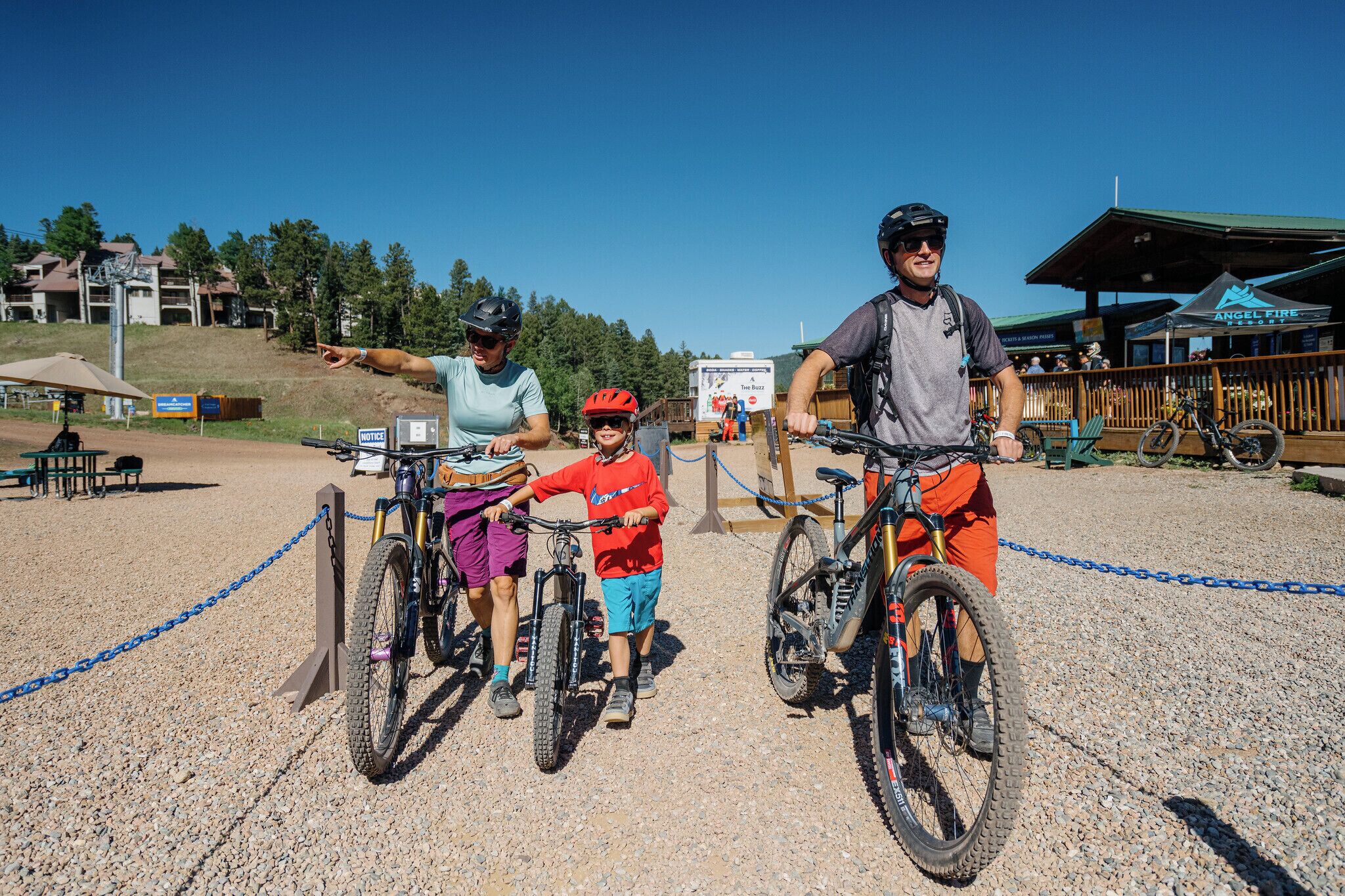 A gravel area with bicycles, a chain barrier, and a building with a sign 'Angel Fire.'