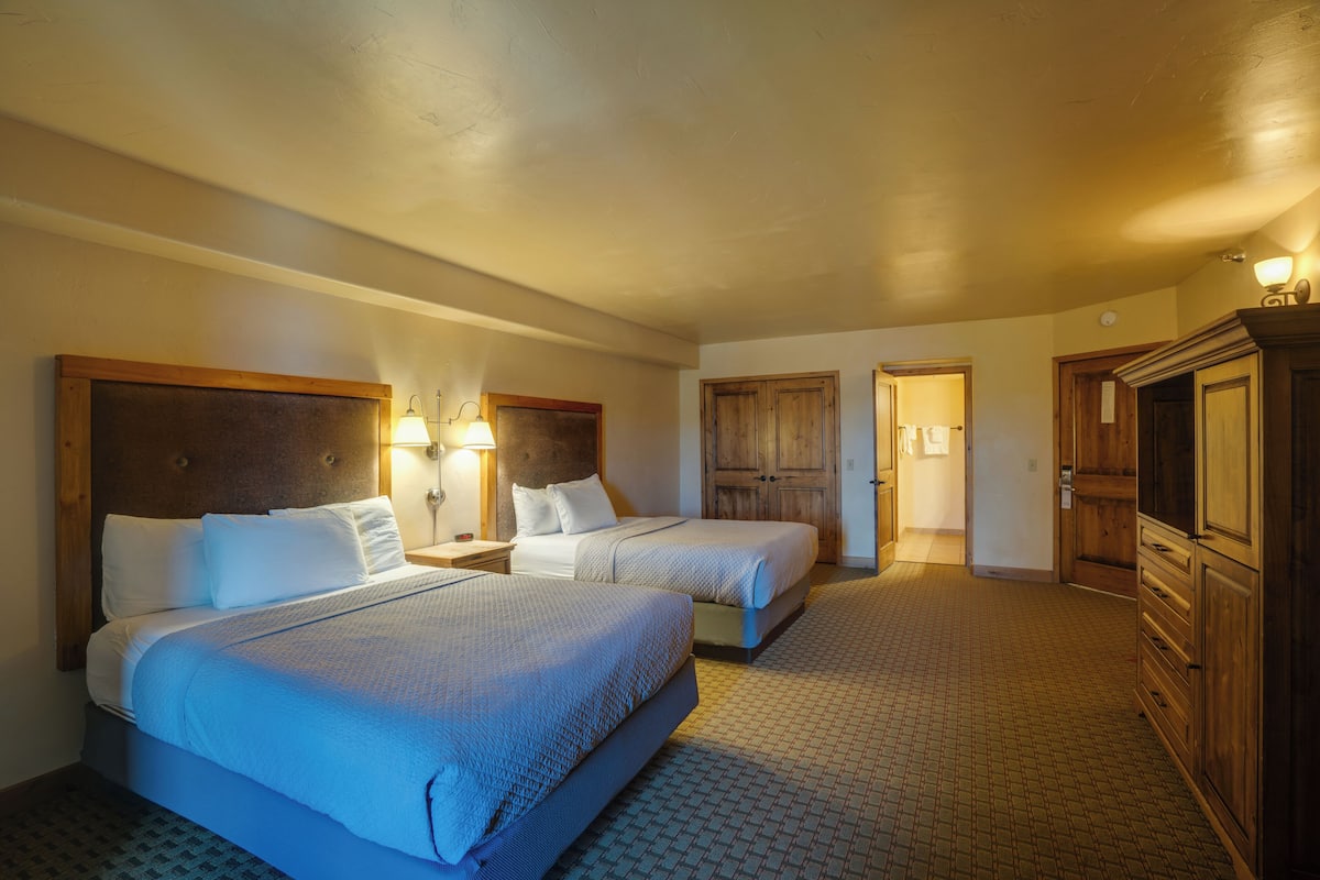 A hotel room with two beds, a wooden wardrobe, and a bathroom door.