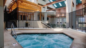 Una piscina interior con una pérgola de madera, una cerca metálica y vistas del interior del edificio.
