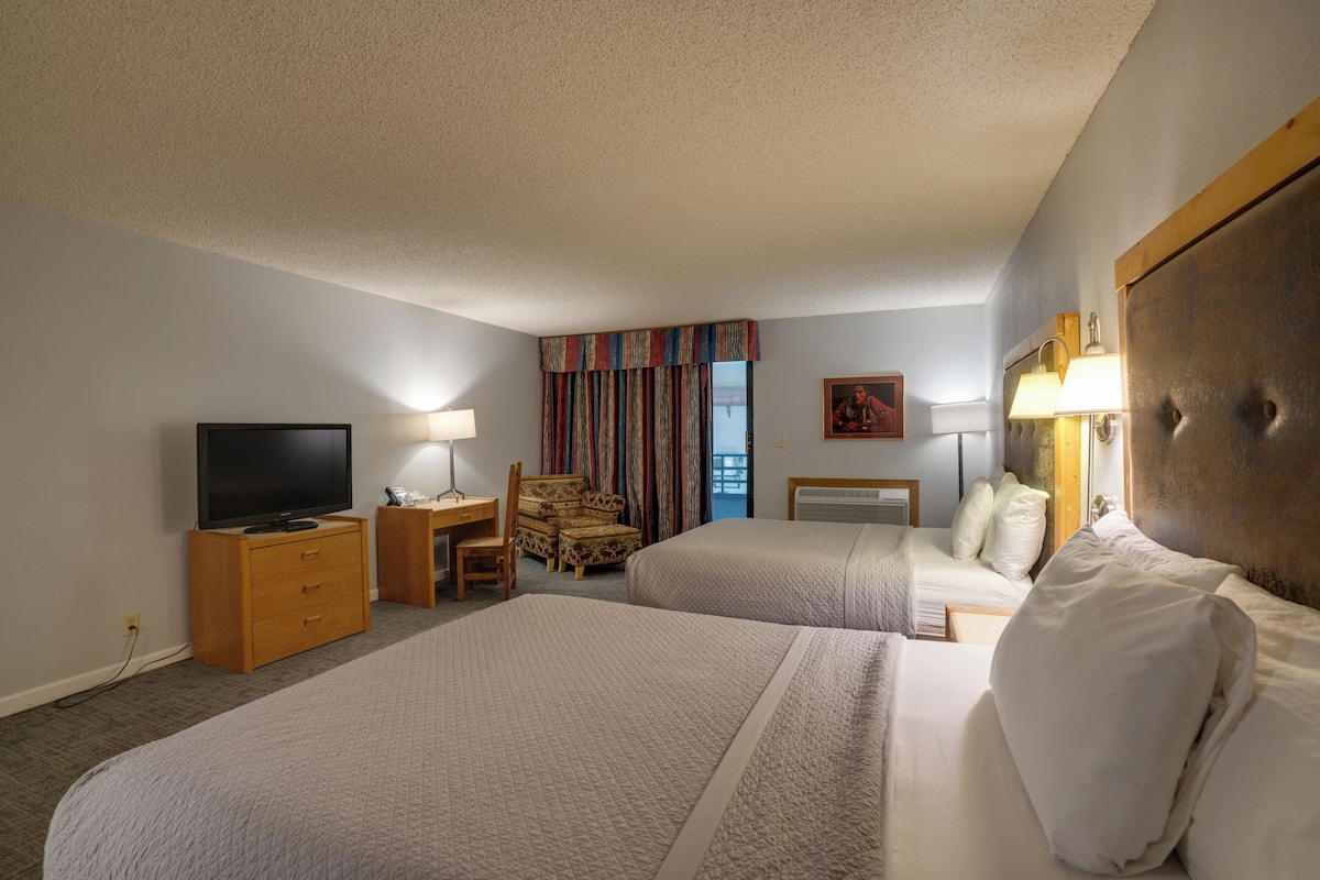 A hotel room with two beds, a desk with a chair, a television, and a window with curtains.