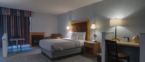 Habitación de hotel con cama, lámparas de noche, escritorio, silla, mesita y chimenea.