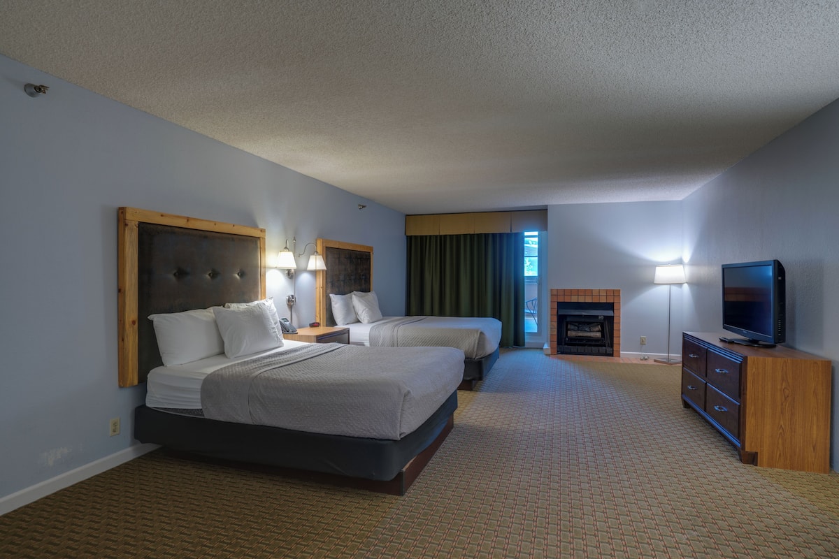 A hotel room with two beds, a television, a fireplace, and a view of the outdoors.