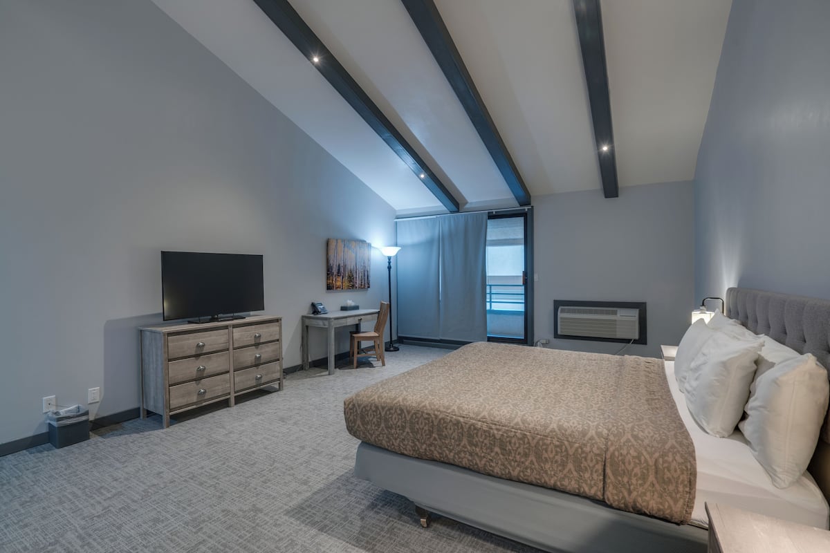 A modern hotel room with a large bed, a desk, a television, and a view of the outdoors.