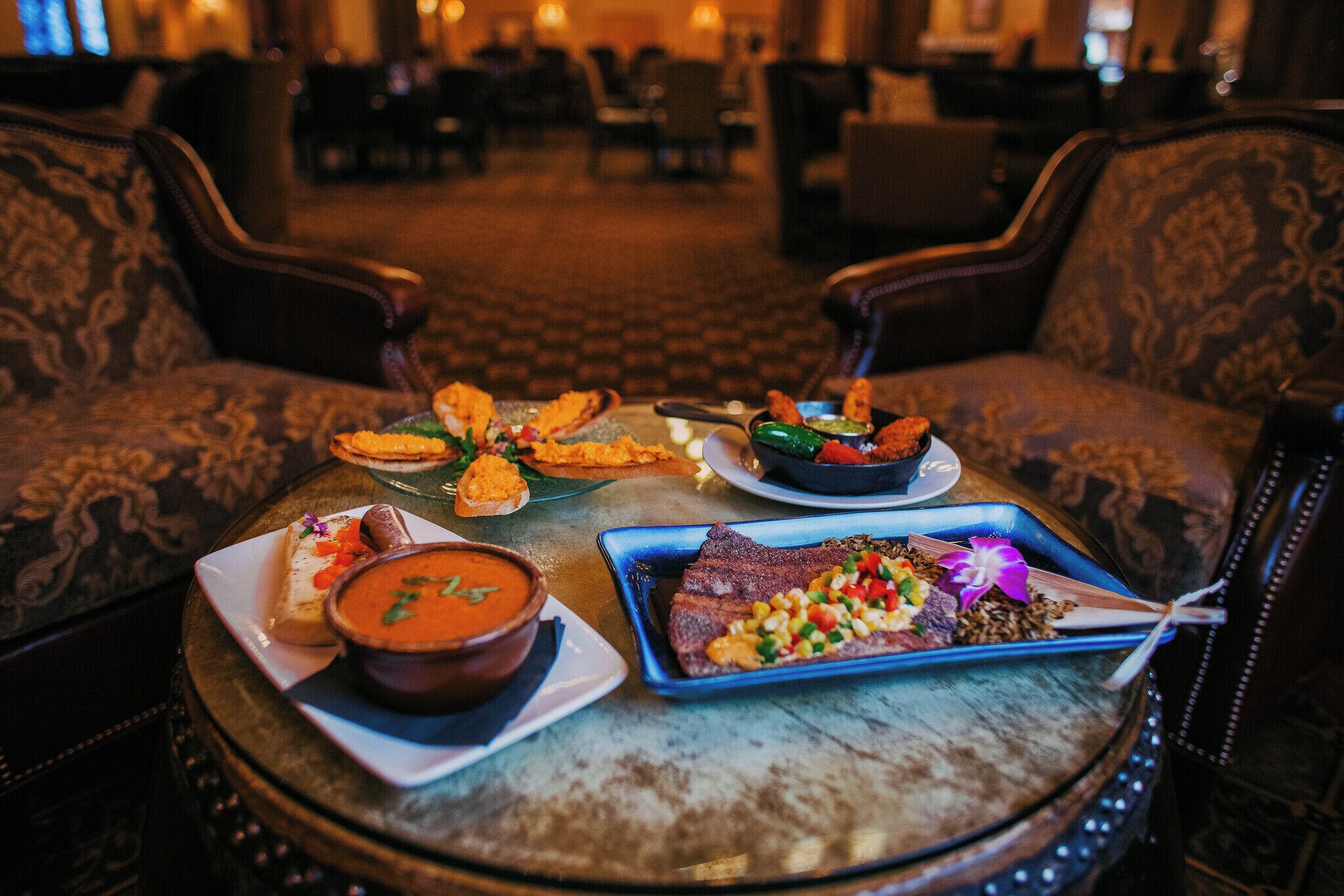 Een eettafel met diverse gerechten, een bank en een kamerbreed tapijt in een hotelhal.