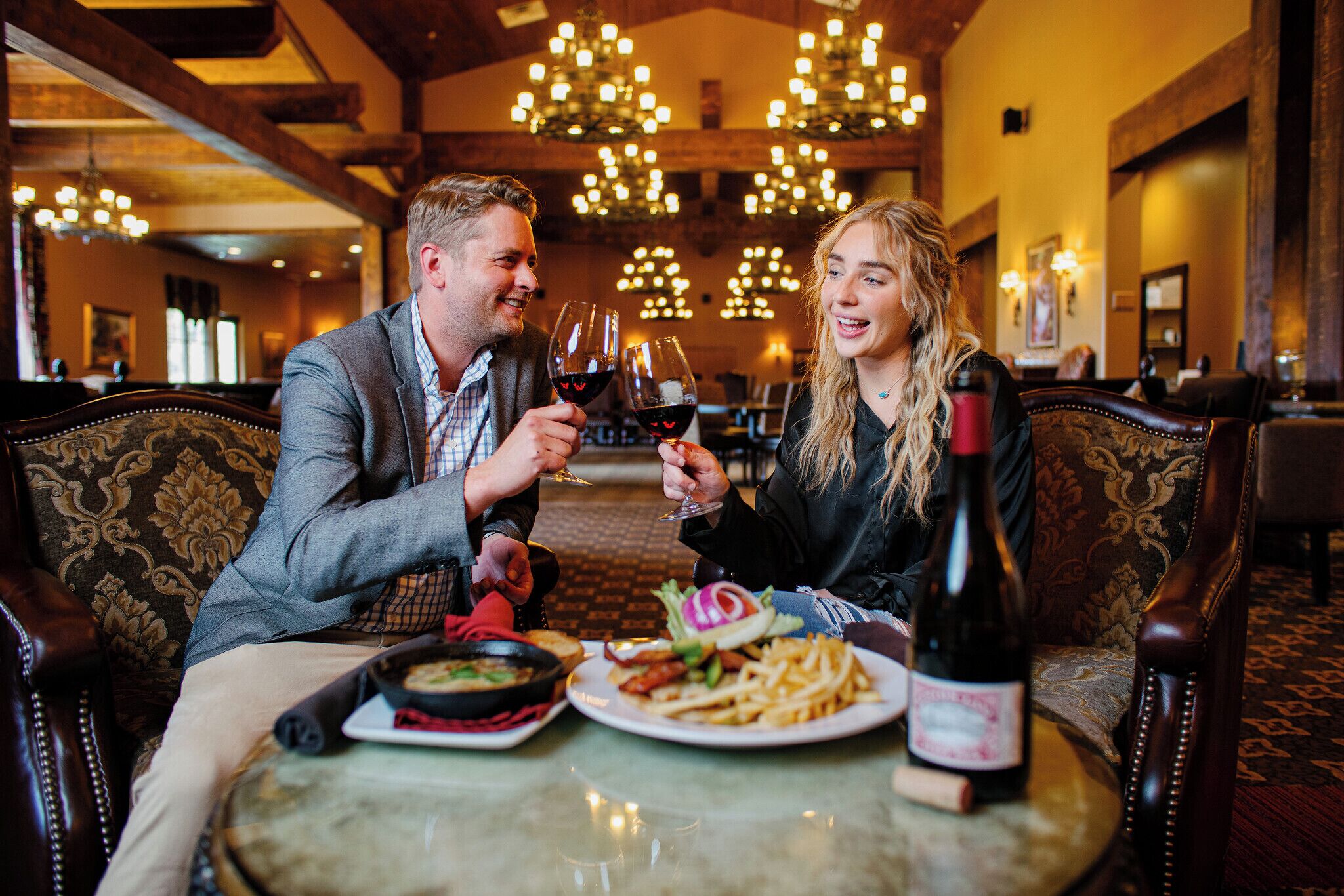 Una pareja sentada a una mesa con una botella de vino, platos de comida y una vela.
