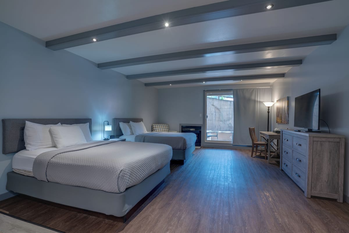 A modern hotel room with two beds, a desk, a TV, and a large window.