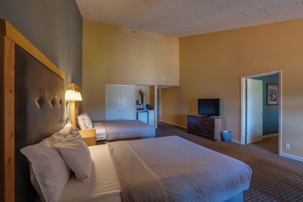 A hotel room with a large bed, a smaller bed, a desk with a television, and a bathroom visible through an open door.