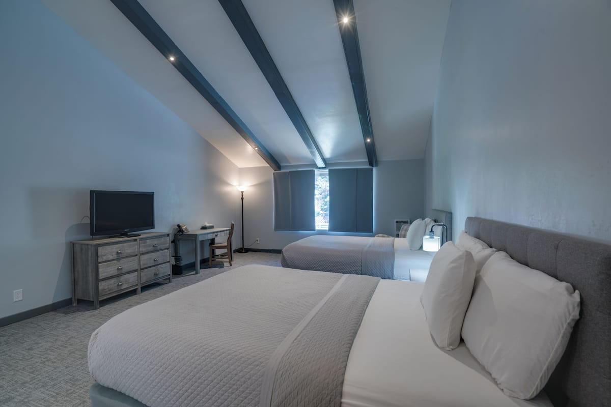 A bedroom with a large bed, a desk, a television, and a window with curtains.