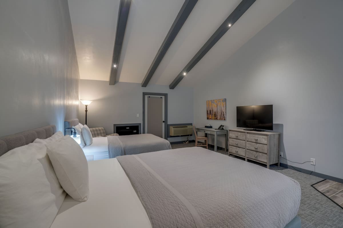 A hotel room with two beds, a desk, a television, and a window.