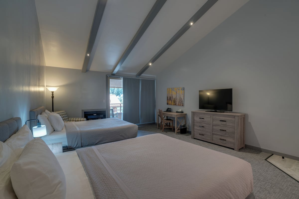 A modern hotel room with two beds, a desk, a television, and a large window.