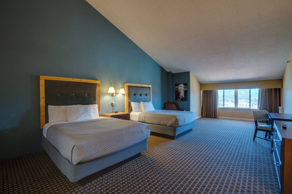 A hotel room with two beds, a desk, and a chair.