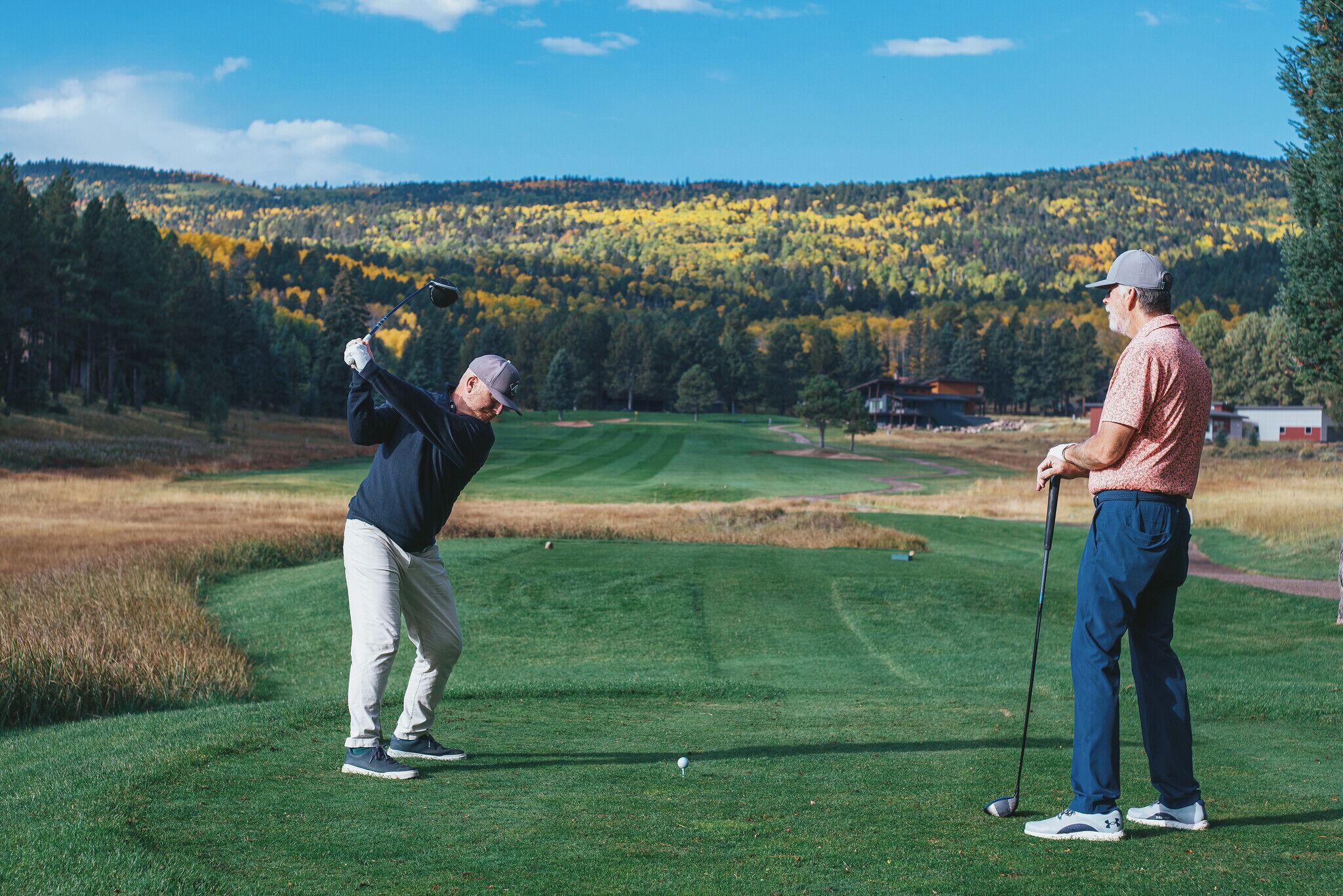 A golf course with a clear sky and autumn trees in the background.